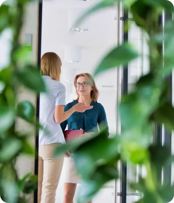 deux femmes en pleine conversation dans un espace professionnel lumineux, vues à travers un encadrement de plantes